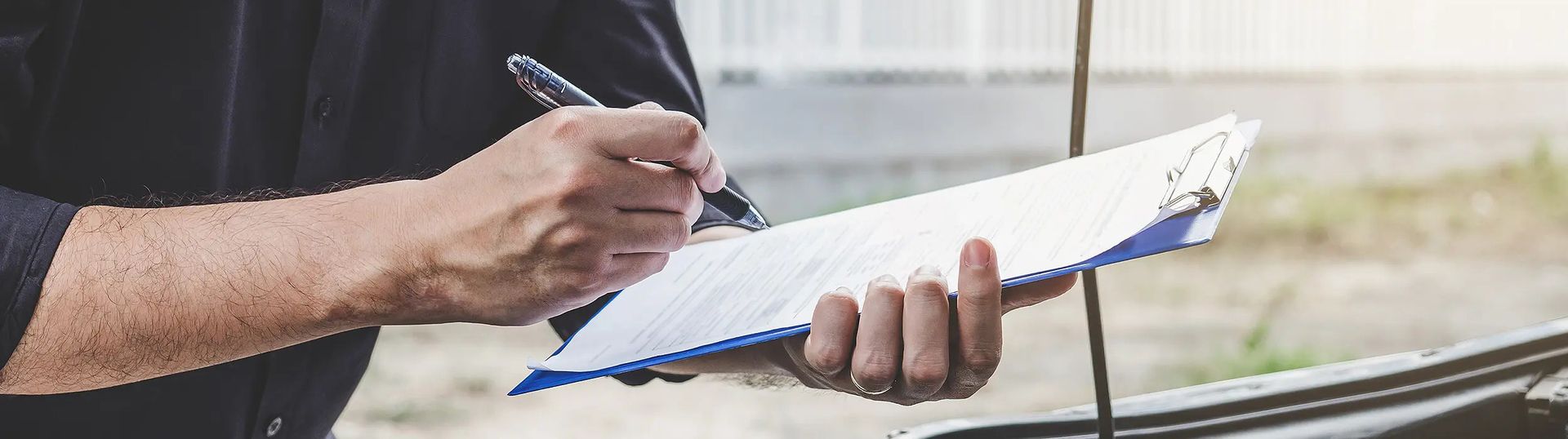 Man sieht den Arm eines Mannes, der ein Schreibbrett hält und ein Unfallgutachten protokolliert.