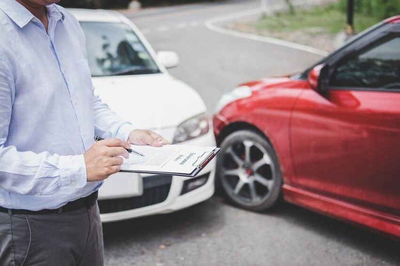 Zwei Fahrzeuge, die in einen Unfall verwickelt sind. Im Vordergrund schreibt ein Mann ein Unfallgutachten.