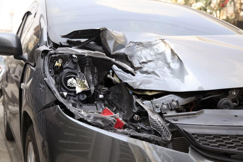 Linke Front eines grauen Fahrzeugs mit einer beschädigten Lampe nach einem Unfall.